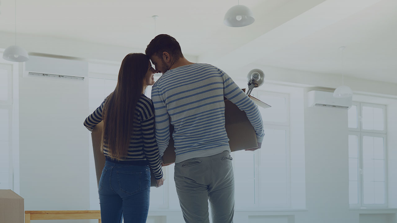 A couple holding moving boxes in a mostly empty room.