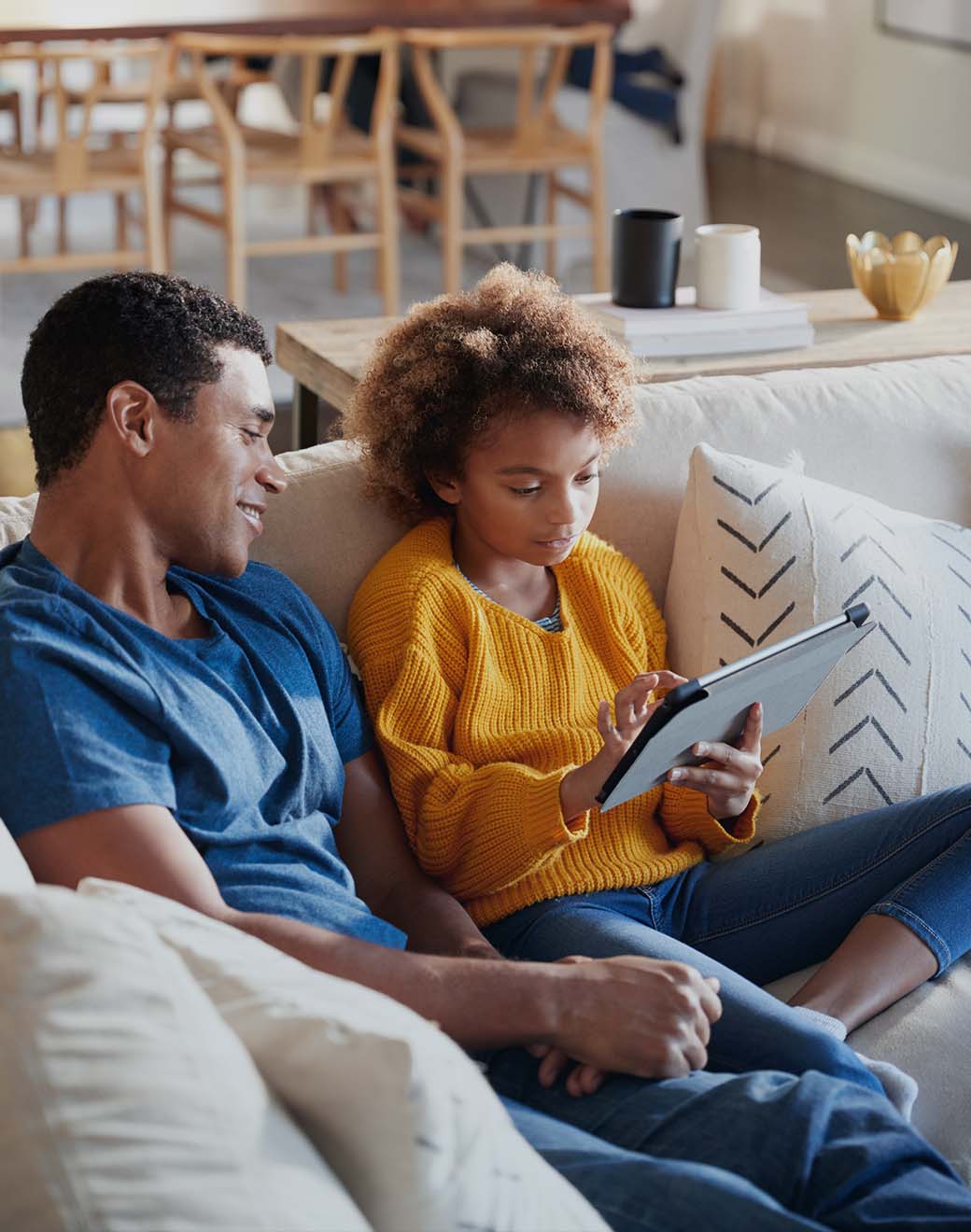 A father and child looking at an iPad together on the couch.