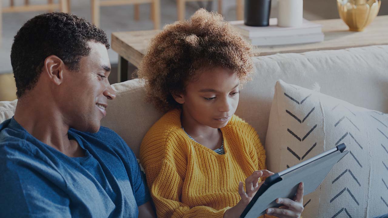 A father and child looking at an iPad together on the couch.